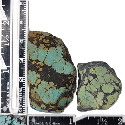 A pair of natural turquoise stones weighing 28 grams, featuring vibrant blue-green hues with intricate golden and dark matrix patterns. The stones measure approximately 4.5 cm x 3.5 cm and 3 cm x 2.5 cm, displayed alongside a ruler for scale. Available for purchase at www.naturalturquoise.com, ideal for lapidary and jewelry projects.