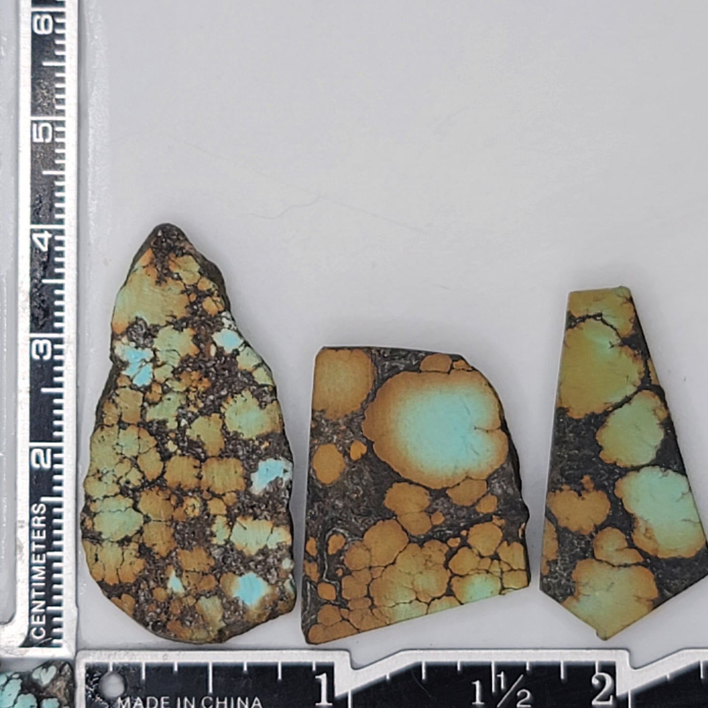 A natural turquoise stone triplet weighing 18 grams, featuring golden tones with vibrant blue highlights and bold dark matrix patterns. The stones measure approximately 4.5 cm x 2.7 cm, 3.8 cm x 2.5 cm, and 3.5 cm x 2 cm, displayed with a ruler for scale. Available for purchase at www.naturalturquoise.com, ideal for jewelry making and lapidary projects.