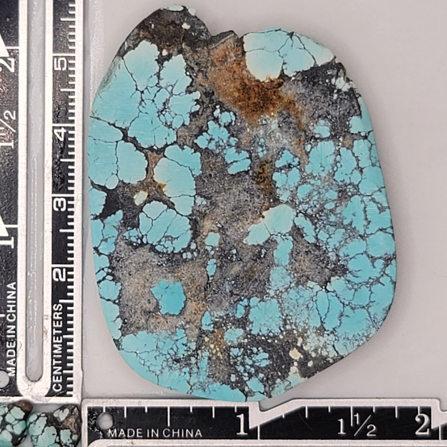 A natural turquoise stone weighing 32 grams, featuring vibrant blue hues with bold dark matrix patterns and earthy textures. The stone measures approximately 5.8 cm x 4 cm x 0.7 cm, displayed with a ruler for scale. Available for purchase at www.naturalturquoise.com, ideal for lapidary and jewelry projects.