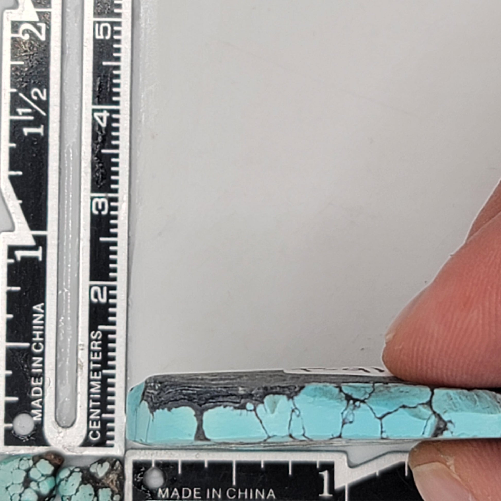 A natural turquoise stone weighing 32 grams, featuring vibrant blue hues with bold dark matrix patterns and earthy textures. The stone measures approximately 5.8 cm x 4 cm x 0.7 cm, displayed with a ruler for scale. Available for purchase at www.naturalturquoise.com, ideal for lapidary and jewelry projects.