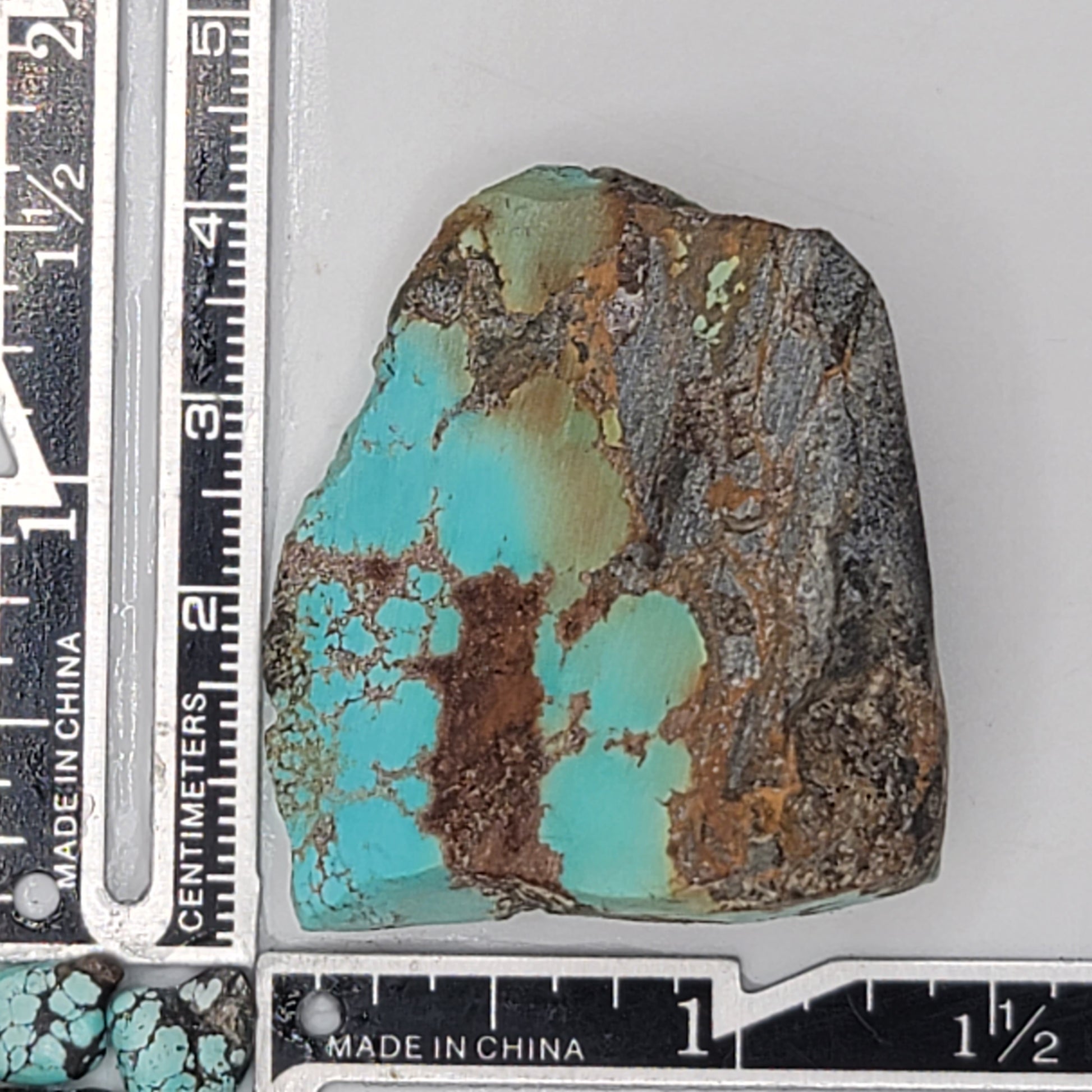 A natural turquoise stone weighing 39 grams, featuring vibrant blue-green tones with warm earthy accents and a bold dark matrix. The stone measures approximately 5.5 cm x 4 cm x 0.8 cm, displayed with a ruler for scale. Available for purchase at www.naturalturquoise.com, perfect for lapidary and jewelry projects.